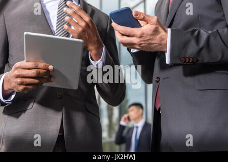 Multiculturale di riunioni di team aziendali e utilizza lo smartphone e tablet digitale all'aperto vicino edificio per uffici Foto Stock