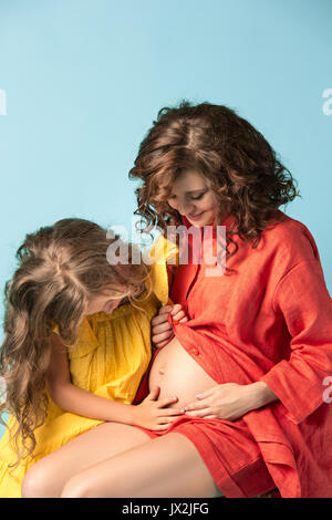 Donna incinta con teen figlia. Studio familiare ritratto su sfondo blu Foto Stock