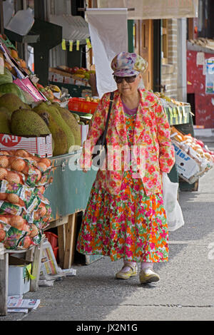 Un vecchio americano asiatico donna in abiti colorati e pressoché a riscontro di camicia, fuori shopping on 73rd Street a Jackson Heights, Queens, a New York. Foto Stock