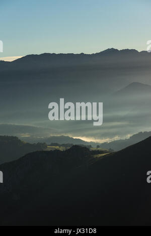 La mattina presto l'alba sul Cabrales valley con la nebbia e il fumo degli incendi in abitazioni locali cast di luce straordinari, Picos de Europa, Asturias, Spagna. Foto Stock