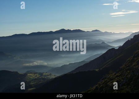 La mattina presto l'alba sul Cabrales valley con la nebbia e il fumo degli incendi in abitazioni locali cast di luce straordinari, Picos de Europa, Asturias, Spagna. Foto Stock