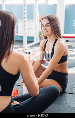 Fitness, sport, della formazione, della palestra e del concetto di stile di vita - due donne sorridente seduto sulla mezza palla e per rilassarsi dopo le lezioni in palestra Foto Stock