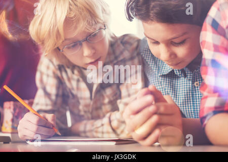 Ragazzo attento a spiare il compito finito del suo amico Foto Stock