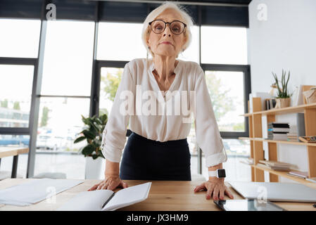 Grave donna intelligente appoggiata sul tavolo Foto Stock