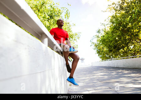 Giovani afro-americane runner nella città seduto sul muro di cemento in possesso di una calzatura, di riposo. Foto Stock