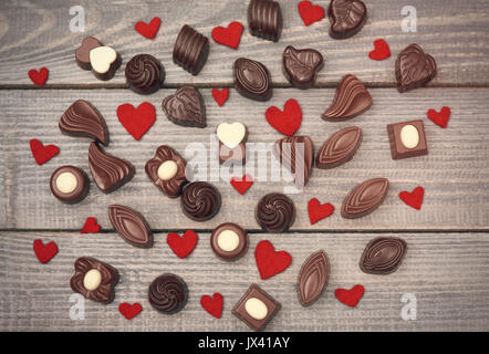 Molti cioccolatini e cuori di feltro sul tavolato in legno Foto Stock