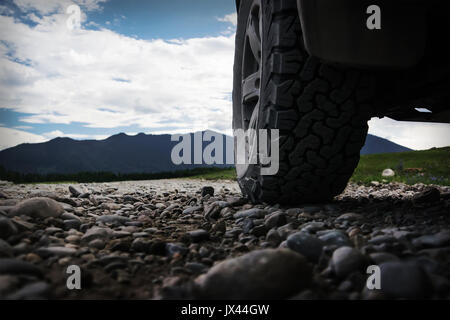 Off-road viaggio su strada di montagna. La ruota del SUV in primo piano, sulla strada di pietra di ghiaia. Foto Stock