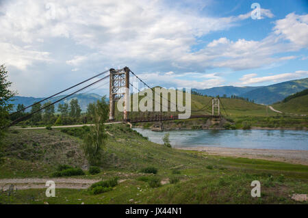 Sospensione ponte attraverso il fiume di montagna, luce della sera, cielo blu Foto Stock