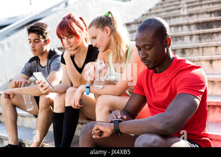 Giovane e bella corridori nella città insieme seduta sulle scale, guardando orologio intelligente o smart phone, tenere traccia dei suoi progressi in esecuzione. Foto Stock