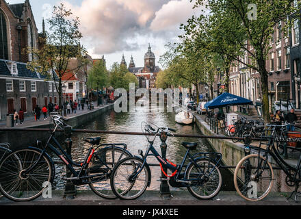 Amsterdam, Paesi Bassi - 25 April, 2017: Biciclette parcheggiate lungo il ponte. Quartiere a luci rosse de Wallen, Vista della Basilica di San Nicola in vigilia Foto Stock