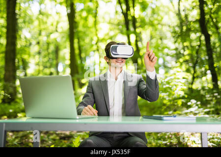 Fiducioso bello uomo d affari con occhiali per realtà virtuale con punta il dito in ufficio escursioni nel verde del parco. Foto Stock