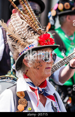 Ritratto di donna matura tradizionale ballerino folk dal Dead Horse morris lato. Indossare occhiali da sole e cappello con grandi piume, e il pattern dipinto sul volto. Foto Stock