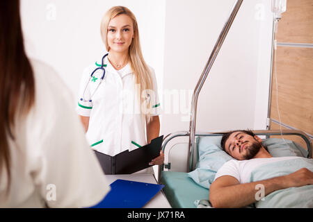 Paziente in stanza di ospedale accanto a due infermieri Foto Stock