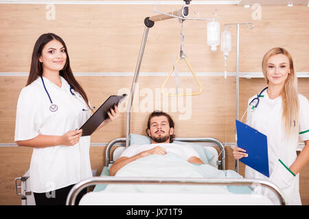 Paziente in stanza di ospedale accanto agli infermieri Foto Stock