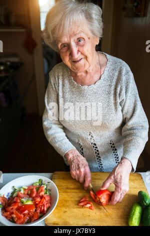 Una donna anziana trita verdure per insalata. Foto Stock