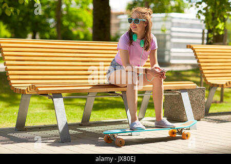 Felice ragazza adolescente con cuffie e longboard Foto Stock