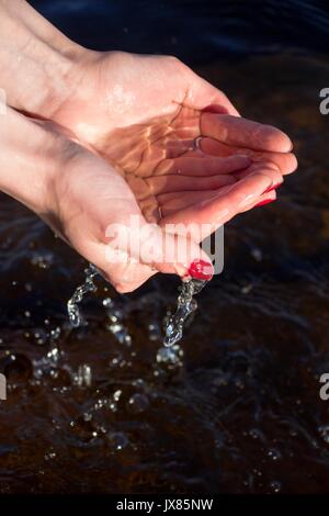 In mani femminili acqua dal lago scorre verso il basso dal palm Foto Stock