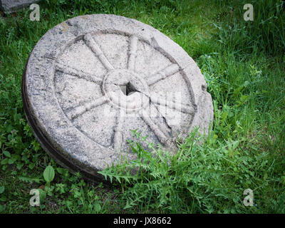 Pietra di granito ruota con metallo arrugginito isolato di RIM sull'erba verde. Foto Stock