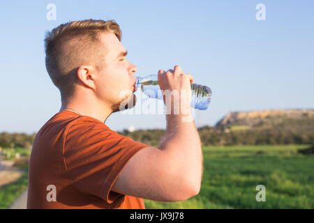Closeup Ritratto di giovane ragazzo acqua potabile dalla bottiglia in una calda giornata di sole Foto Stock