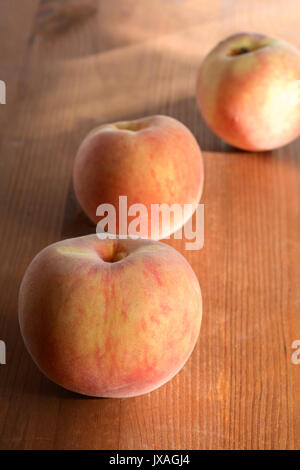 Tre freschezza di frutta pesche giacente su una superficie di legno Foto Stock