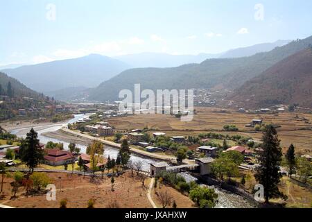 Ponte che attraversa il fiume con il tradizionale stile Bhutanese case a valle di Paro, Bhutan Foto Stock