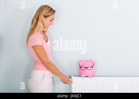 Donna sorridente termostato di regolazione per ridurre il riscaldamento per risparmiare denaro sulla bolletta energetica Foto Stock