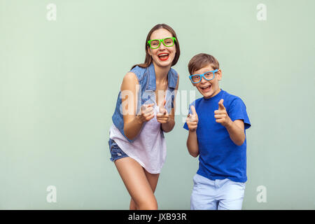 Emozioni e sentimenti. Hey! Il freckled fratello e sorella in casuale t shirts indossando occhiali trendy e posa su sfondo verde chiaro toget Foto Stock