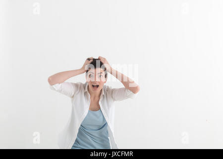 Giovane donna gridando di terrore con le mani sul suo capo, la bocca spalancata cercando in panico alla fotocamera. Close up ritratto di donna irritata gridando, coprendo i suoi orecchi, arrabbiato con i vicini rumorosi Foto Stock