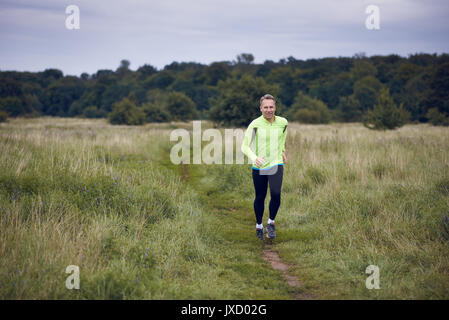 Montare l'uomo muscolare jogging su un sentiero rurale attraverso prati di indossare abbigliamento sportivo in uno stile di vita attivo concept Foto Stock