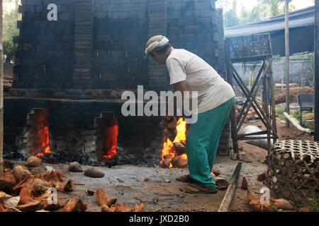 Mattone tradizionale forno usando gusci di noce di cocco per il carburante a Bali, in Indonesia con un lavoratore di gettare in gusci di noce di cocco in al fuoco Foto Stock