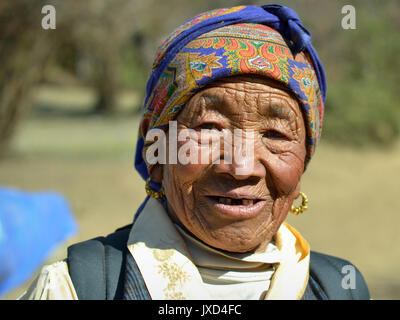 Vecchia donna Sherpa con faccia viva e tradizionali orecchini dorati pone per la macchina fotografica. Foto Stock