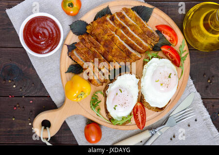 Pezzi di chop (cotoletta), toast con uova, pomodoro fresco su una tavola di legno su uno sfondo scuro. Vista dall'alto. Foto Stock