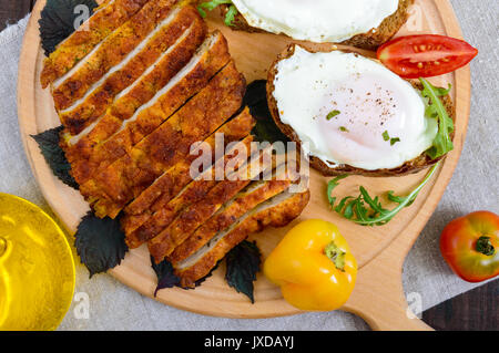 Pezzi di chop (cotoletta), toast con uova, pomodoro fresco su una tavola di legno su uno sfondo scuro. Vista dall'alto. Foto Stock