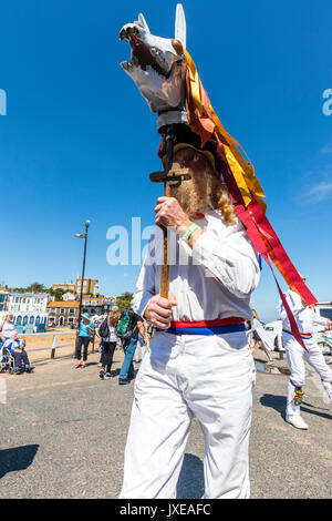 Inghilterra, Broadstairs Settimana della musica folk. Madcap Morris bestia dancing in bright sole estivo. La tenuta di un teschio di animale su un palo sopra la sua testa con orange streamers sospeso verso il basso . Foto Stock