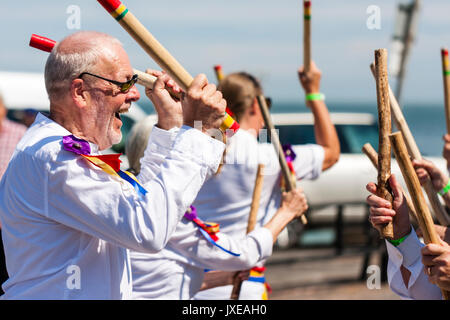 Inghilterra, Broadstairs settimana della musica folk. Tradizionale ballerini folk, Madcap morris dancing laterale sul molo del porto. Close up, testa e spalle, laughing man tenere due bastoni con altri bastoni che si terrà nell'immagine. Foto Stock