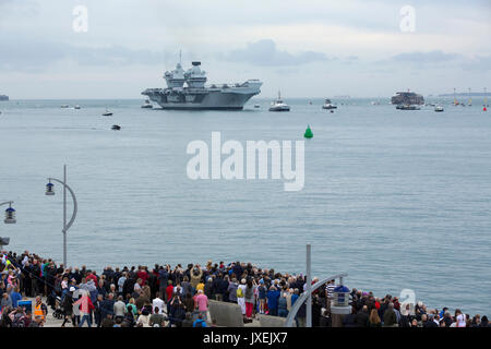HMS Queen Elizabeth la vela in Portsmouth è la porta di casa per la prima volta. Grandi nuvole raccolti presto su un grigio estati nuvoloso giorno. Foto Stock