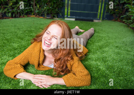 Bellissimi i capelli rossi donna giace sul prato e prende piacere nel suo giardino Foto Stock