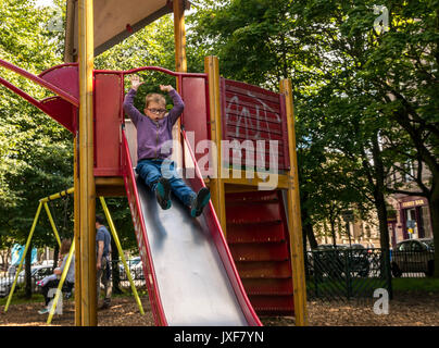 I giovani disabili ragazzo con gli occhiali e la fibra di carbonio tutore gamba essendo brave andando giù scorrere nel parco giochi avventura, Leith, Edimburgo, Scozia, Regno Unito Foto Stock