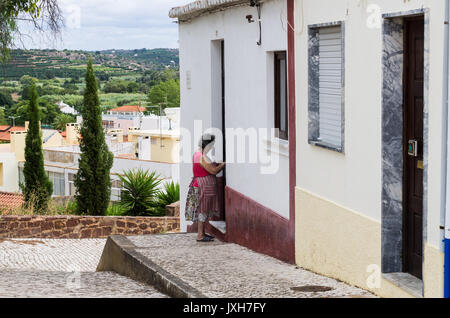 Vecchia donna di apertura di una porta di una casa su una strada, Silves, Algarve, PORTOGALLO Foto Stock