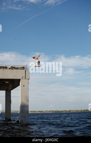 Un uomo è il salto in mare da un molo di alta. Adrenalina e extreme. Torna capriola in salto. Foto Stock