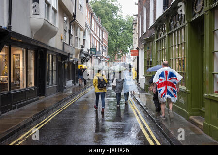 Molto giorno piovoso nel centro di York, indicato con ombrelloni e un uomo in un unione bandiera giacca a vento poncho Foto Stock