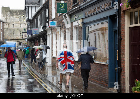 Molto giorno piovoso nel centro di York, indicato con ombrelloni e un uomo in un unione bandiera giacca a vento poncho Foto Stock