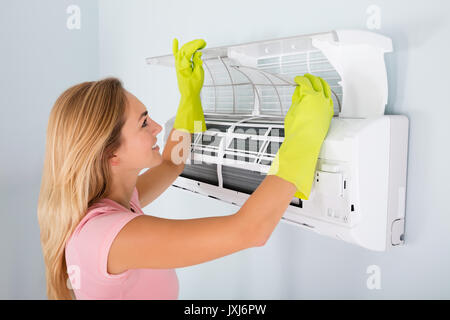 Giovane donna Pulizia sistema di aria condizionata a casa Foto Stock