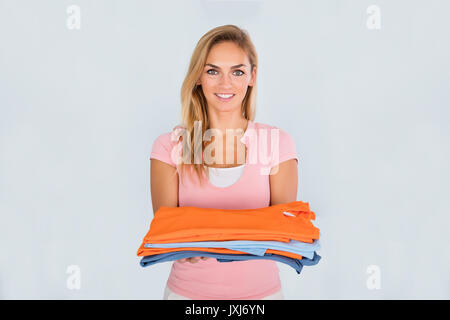 Ritratto di una giovane donna sorridente tenendo un mucchio di vestiti stirati Foto Stock