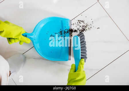 Close-up della persona che indossa guanti spazzare il pavimento con la scopa e paletta Foto Stock