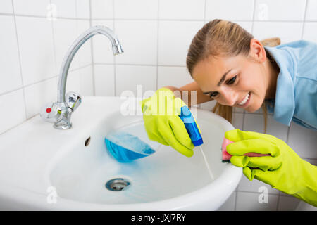 Close-up di Donna sorridente Pulizia del bacino con la bottiglia spray e spugna in bagno Foto Stock