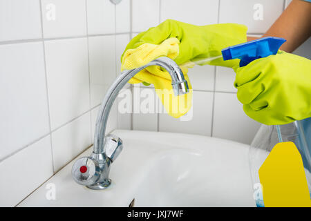 Close-up di donna mano nella pulizia dei guanti il rubinetto del lavandino con spugna in bagno Foto Stock