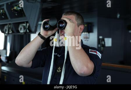 Un membro di equipaggio utilizza il binocolo per guardare fuori in mare dal ponte sul bordo HMS Queen Elizabeth mentre si prepara a entrare nel suo home porto di Portsmouth per la prima volta il mercoledì. Foto Stock