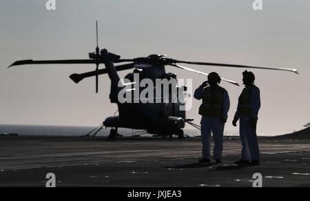 I membri dell'equipaggio accanto ad un elicottero Merlin a bordo HMS Queen Elizabeth mentre si prepara a entrare nel suo home porto di Portsmouth per la prima volta il mercoledì. Foto Stock