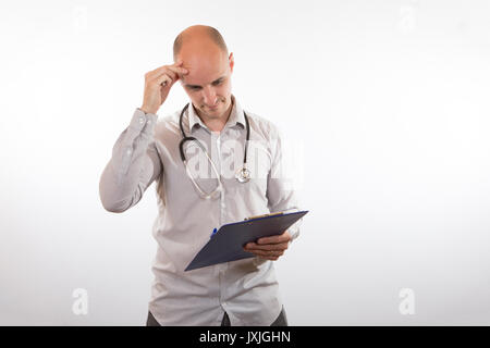 Riflessivo medico di graffiare la sua testa come egli rappresenta la lettura di un insieme di note paziente su un blocco appunti su bianco con spazio di copia Foto Stock